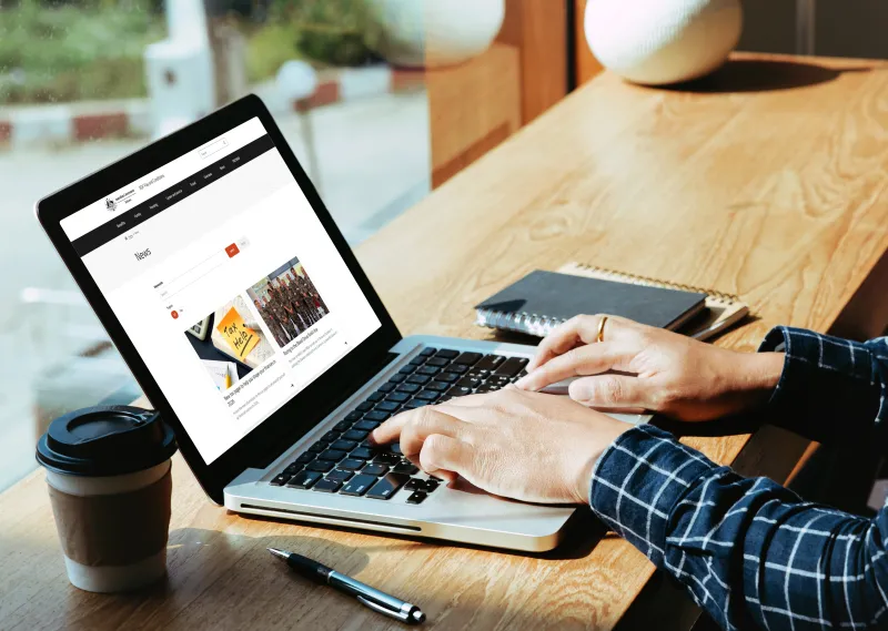 A man sitting at a café bench with an open laptop in front of him, displaying the new ADF Pay and Conditions news webpage 
