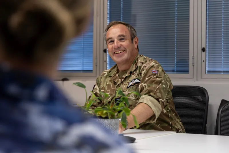 A Royal Air Force Air and Space Commander sits across a desk, smiling at a RAAF soldier who has their back to the camera