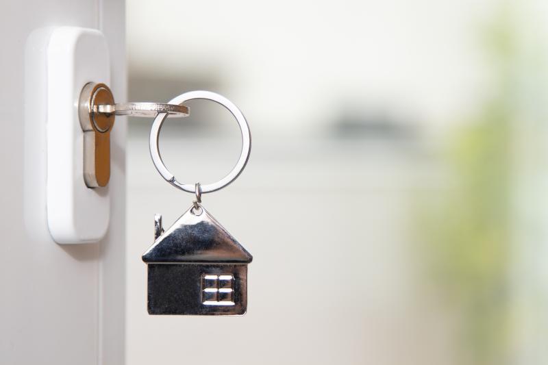 An open front door of a house with a key in the lock that has a keyring hanging from it shaped like a house