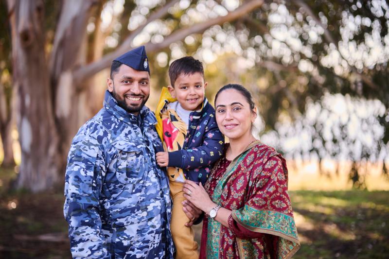An Air Force member standing with his wife and young son, in front of a large gum tree.  